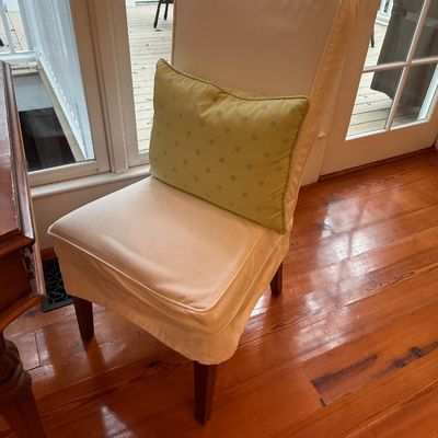 Contemporary armless dining chair featuring a cream-colored fabric slipcover and dark wood legs, paired with a green polka-dot accent...