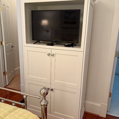 Contemporary white wood entertainment cabinet featuring an open upper shelf housing a flat-screen television above four panel cabinet...