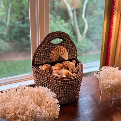 Handcrafted shell-encrusted basket filled with mixed seashells, flanked by two specimens of natural white coral on acrylic stands.