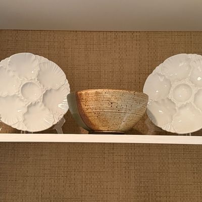 Pair of white glazed ceramic oyster plates displayed alongside an studio pottery bowl on a shelf.