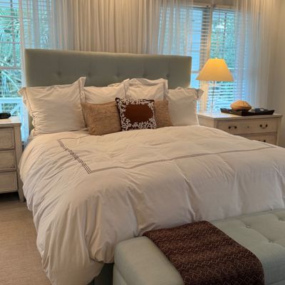 Upholstered light blue king-size bed frame with a tufted headboard, dressed in white bedding, complemented by a matching tufted storage...