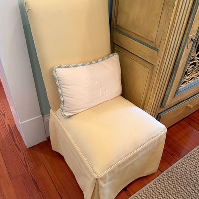 Fully upholstered pale yellow dining accent chair featuring a skirted base and an embroidered accent pillow.