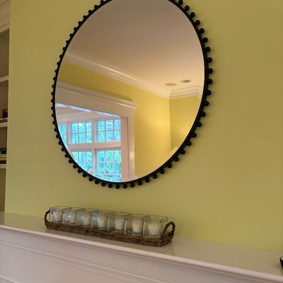 Contemporary round wall mirror with a beaded dark metal frame mounted above a white fireplace mantel.