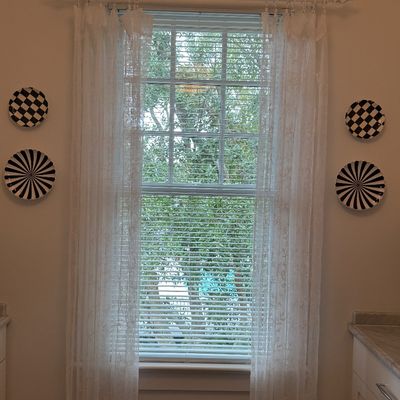Set of four MacKenzie-Childs style black and white pattern decorative wall plates mounted on either side of a window with white sheer...