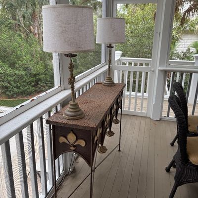 Rustic wrought iron console table featuring fleur-de-lis accents, paired with a matching set of slender buffet lamps with fabric shades.