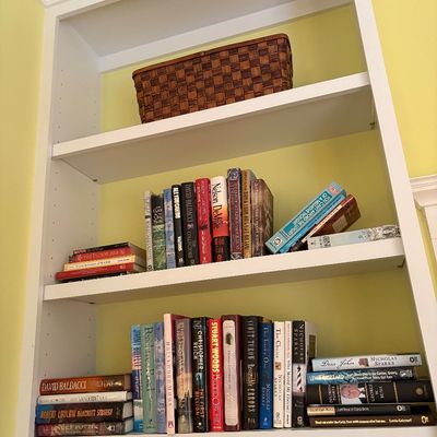 White built-in bookcase filled with assorted hardcover and paperback fiction and non-fiction books, topped with a woven storage basket.