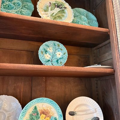 Collection of vintage French majolica ceramic decorative plates, featuring asparagus motifs, floral patterns, and oyster plates displayed...