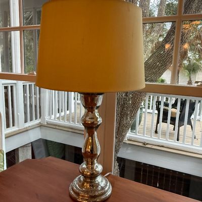 Mercury glass table lamp with a baluster-style stem and a yellow drum shade, set on a wooden tabletop near a window.