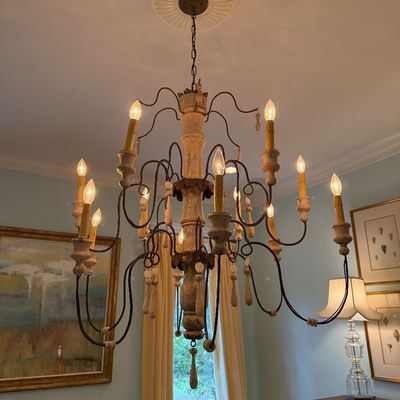 French Country style multi-light chandelier featuring a whitewashed wooden central column and scrolling metal arms with faux candle sleeves.