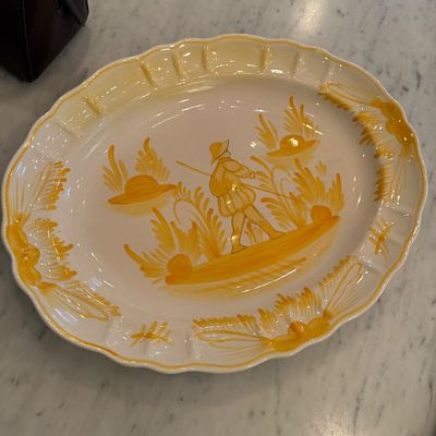 Sale Photo Thumbnail #107: Hand-painted oval ceramic platter featuring a yellow motif of a figure with a staff, Quimper style with scalloped rim.