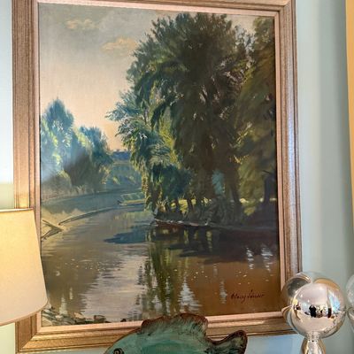 Framed impressionistic landscape oil painting depicting a river scene with lush trees, signed by the artist in the lower right, displayed...