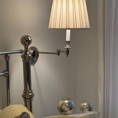 Polished nickel swing-arm wall sconce with a pleated fabric shade mounted near a metal bed frame.