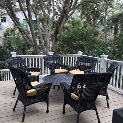 Seven-piece outdoor patio set featuring six black wicker armchairs with tan seat cushions and a matching round metal table, displayed on...
