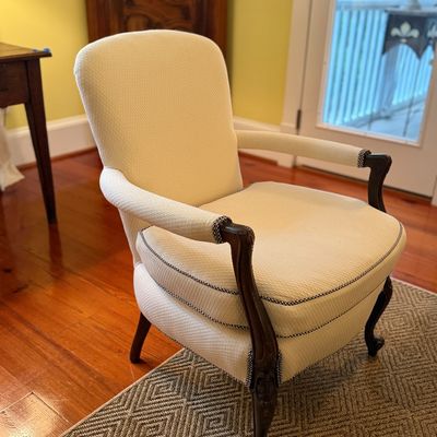 French Provincial style upholstered armchair featuring cream textured fabric with corded piping and carved wood cabriole legs.