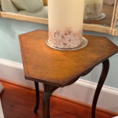 Vintage triangular leather-top side table featuring cabriole legs and a Greek key tooled border, displaying a decorative seashell pillar...
