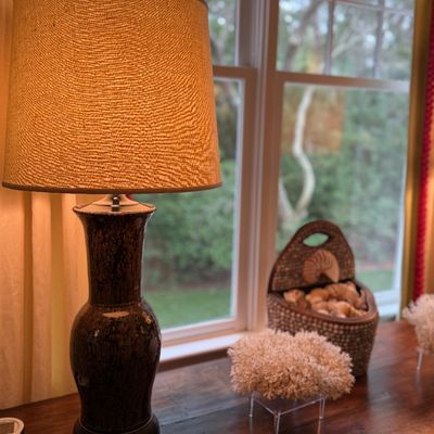 Vintage dark glazed ceramic table lamp with a textured fabric drum shade, displayed alongside coastal decor including a woven basket with...