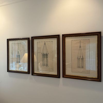 Set of three framed architectural lighting sketches depicting hanging lanterns, presented in matching dark wood frames with cream matting.