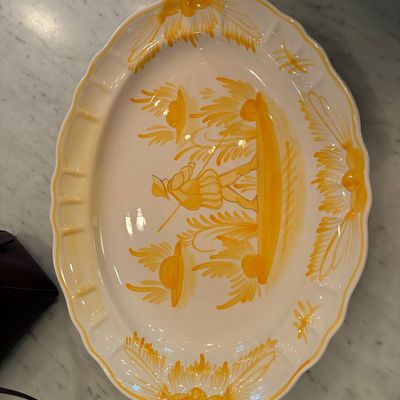 Large oval ceramic serving platter with hand-painted yellow figural motif and decorative rim detailing.