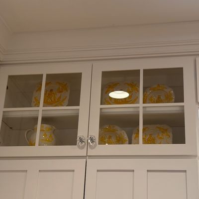 Collection of yellow and white decorated ceramic tableware displayed inside white glass-front kitchen cabinets with crystal knobs.