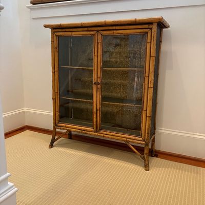 Vintage faux-bamboo and wicker display cabinet with double glass doors, two interior shelves, and a textured backing.
