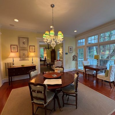 Spacious dining area featuring a round wooden table with chairs, a decorative chandelier, side console table, and large windowed doors.