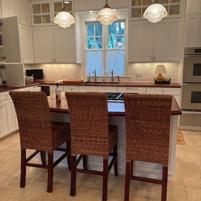 Set of three woven rattan barstools with dark wood legs in a spacious kitchen setting.
