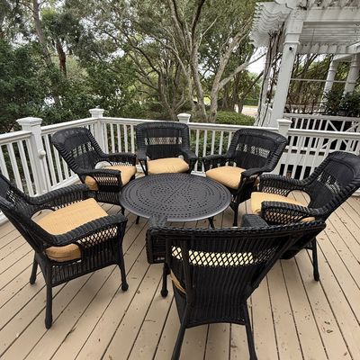 Seven-piece outdoor patio set featuring six black resin wicker armchairs with tan seat cushions and a matching round metal dining table.