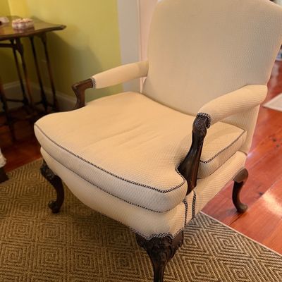 Traditional armchair upholstered in cream fabric with contrast piping trim and carved wood cabriole legs.