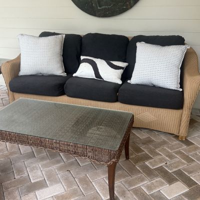 Outdoor patio set featuring a woven wicker sofa with black cushions and decorative throw pillows, alongside a matching glass-top wicker...