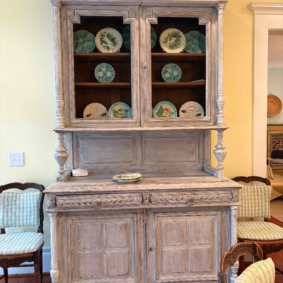 French Country style whitewashed wood hutch with chicken wire cabinet doors, displaying a set of decorative ceramic majolica plates.