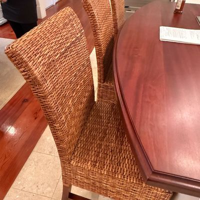 Sale Photo Thumbnail #110: Set of woven rattan high-back dining chairs with wooden legs, arranged around a polished wood table.