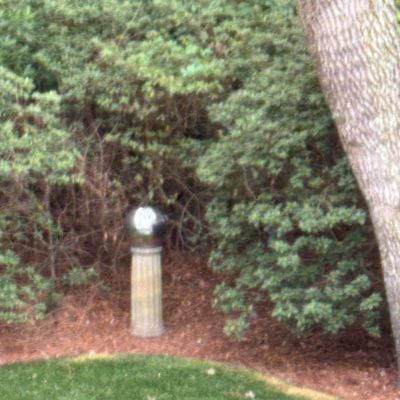 Reflective gazing ball sitting atop a classical fluted pedestal in a garden landscape.