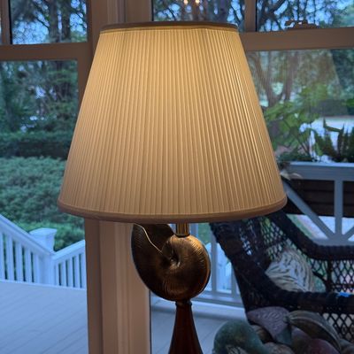 Nautical-themed table lamp featuring a metallic nautilus shell form above a turned wooden pedestal, topped with a pleated fabric shade.