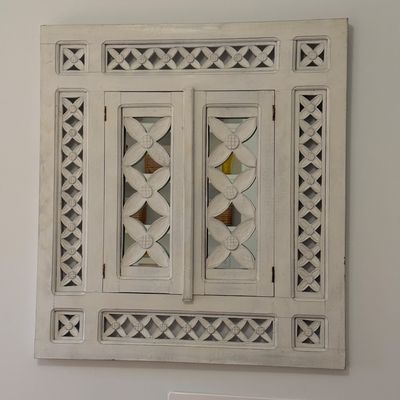 White-washed wood wall mirror featuring carved lattice trim and dual shutter doors with floral cutout designs.