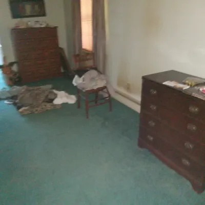 Two vintage wooden dressers and a wooden side chair in a bedroom with teal carpeting.