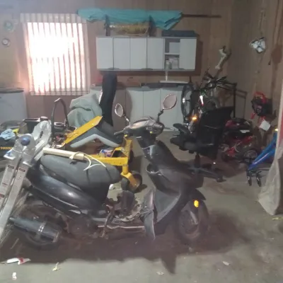 A black motor scooter parked in a garage alongside a yellow riding lawn mower, an aluminum ladder, and various tools.