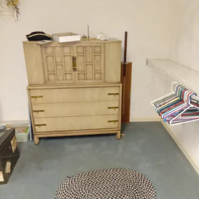 Mid-century modern light wood gentleman's chest with geometric cabinet doors and brass drawer pulls, shown alongside an oval braided...