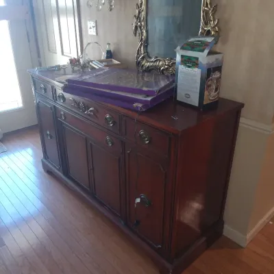 Traditional dark wood sideboard with brass hardware, featuring multiple drawers and cabinets, shown with a gold-framed wall mirror...