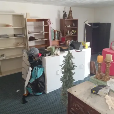 Assorted household items and furniture, including wooden and laminate bookshelves, a white storage cabinet, a golf bag with clubs, and...