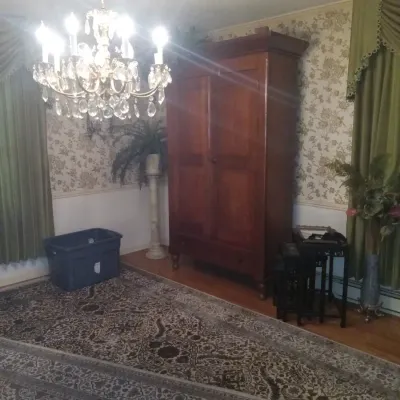 Antique wooden armoire with a single bottom drawer, shown alongside a crystal chandelier and a large patterned area rug.