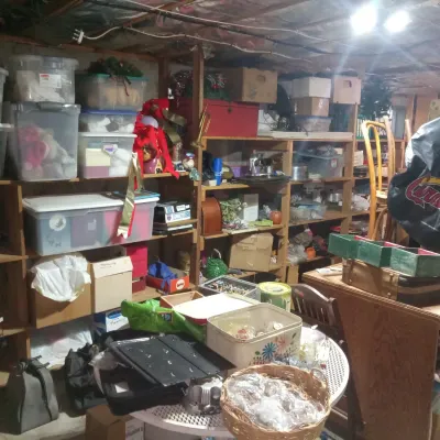 A basement storage area filled with wooden shelving units holding plastic storage bins, cardboard boxes, holiday decorations, and...