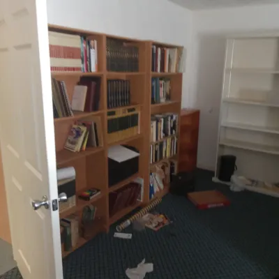 Multiple wooden and laminate bookcases filled with books, binders, and office supplies in a carpeted room.