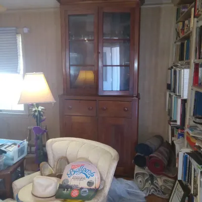 Large wooden hutch with glass-front upper cabinet doors, two drawers, and lower cabinet storage, shown alongside an armchair, floor lamp,...