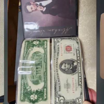 A collection of vintage US currency, including a two-dollar bill and a five-dollar bill, displayed in a protective album alongside...