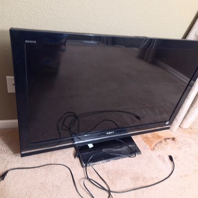 Sale Photo Thumbnail #32: Sony Bravia flat-screen television with a black bezel and stand, shown with power and connection cords.