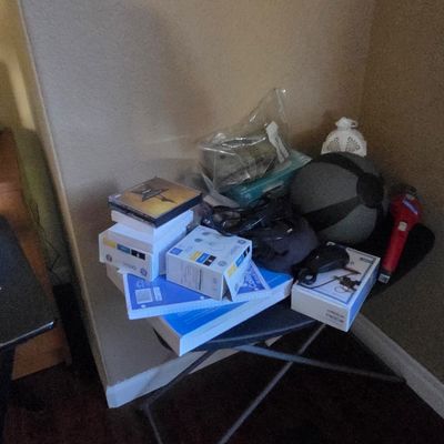 Sale Photo Thumbnail #47: Assorted household items, including printer ink cartridges, notebooks, a medicine ball, and a red flashlight, arranged on a black folding tray table.