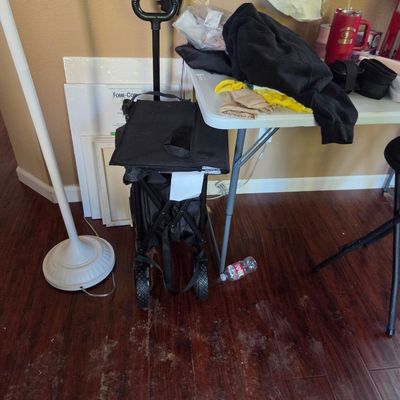 Sale Photo Thumbnail #80: Black folding utility wagon with a telescoping handle, shown in a folded position next to a white folding table.