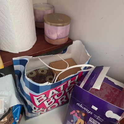 Sale Photo Thumbnail #66: Assorted household items including Bath & Body Works candles, a shopping bag with boxed items, and a box of Always Radiant feminine hygiene products.