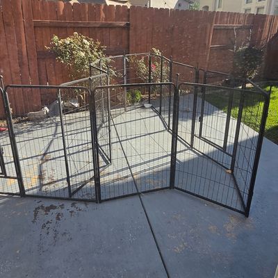 Sale Photo Thumbnail #44: Black metal folding pet playpen set up on a concrete patio, featuring multiple interlocking wire panels and a built-in gate.