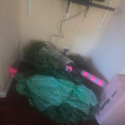 Sale Photo Thumbnail #81: Disassembled artificial Christmas tree wrapped in bubble wrap and storage straps, resting on a dark wood floor.